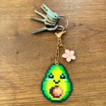 Porte-clé et bijou de sac soré Pixel art en perles thermocollés Avoki l'avocat avec sa fleur de cerisier utilisé en porte-clé avec des clés.