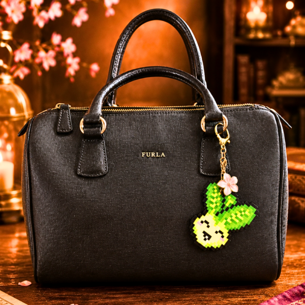 Porte-clé doré en Pixel art Pakou le pak choi en perles thermocollantes avec sa fleur de cerisier rose utilisé en bijou de sac sur un sac à main noir classique.
